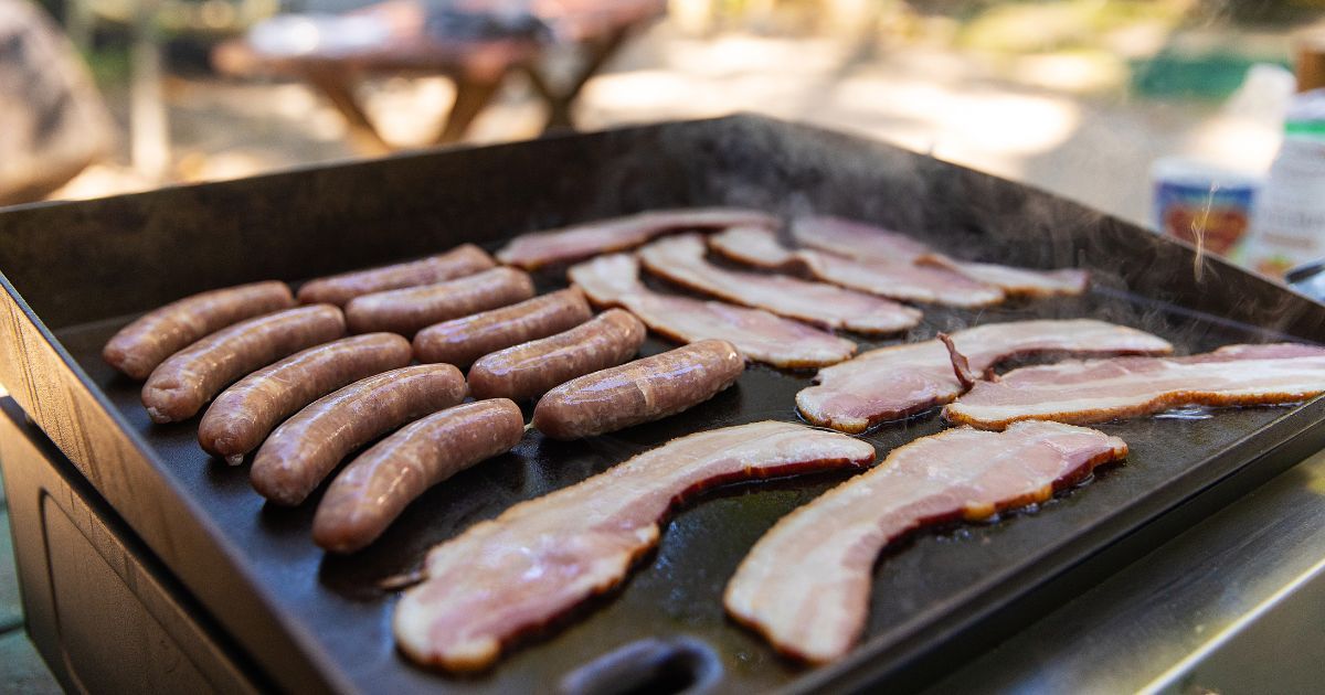 sausage and bacon cooking on a griddle