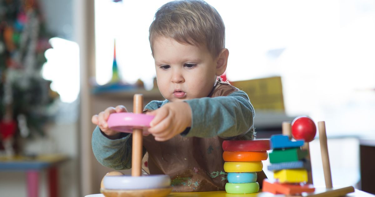 toddler playing with wooden ring stacking game