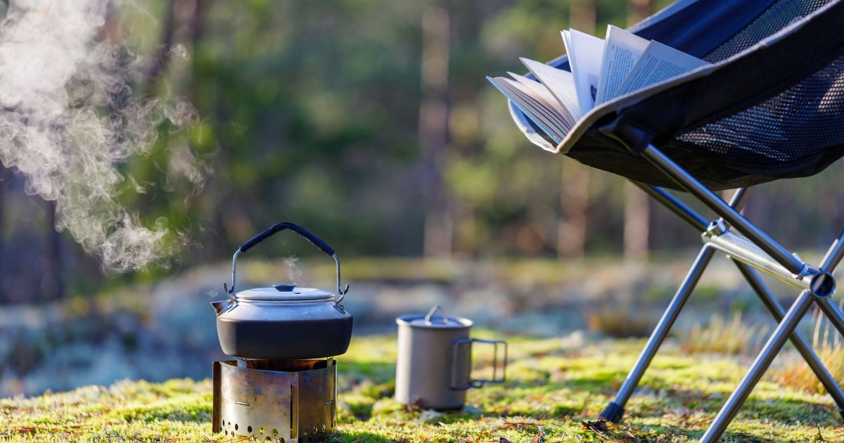 camping kettle boiling on small stove next to camp chair