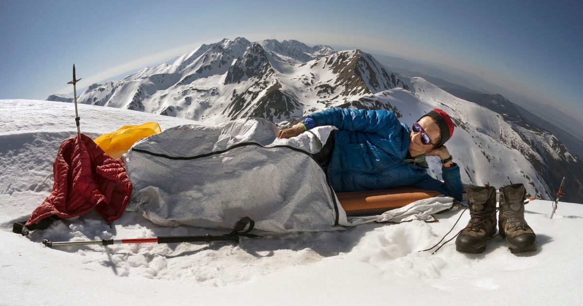 man on top of mountain laying in bivy sack