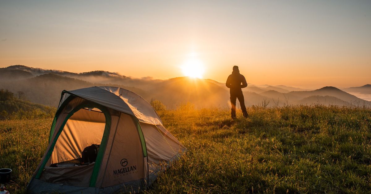 one man tent setup on top of mountain during sunset