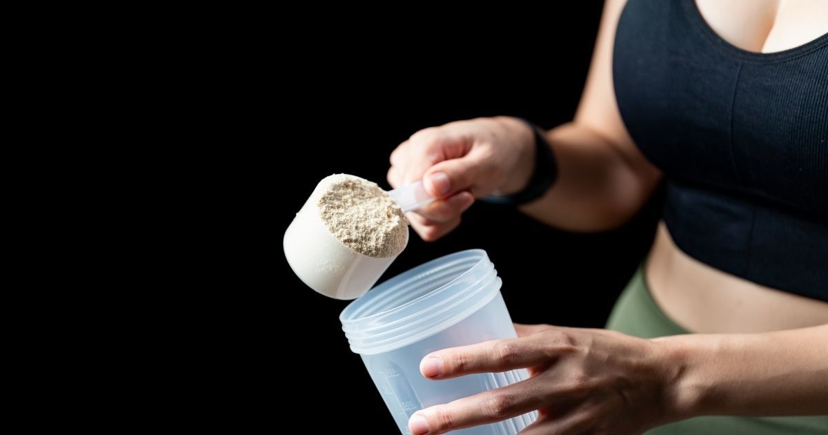 woman putting scoop of protein into shaker cup