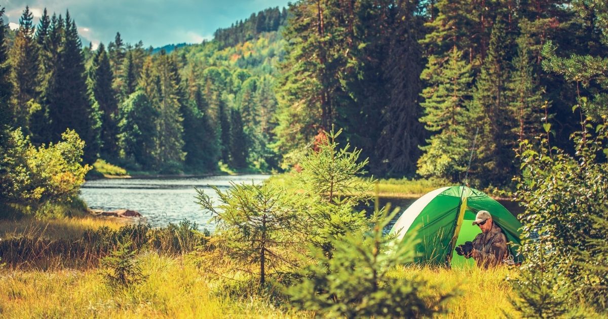 man with tent setup in the forest by a lake