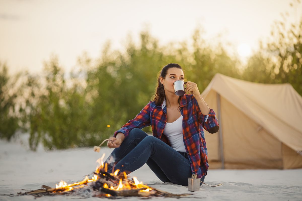 girl sitting by fire, roasting marshmallow, tent in the background